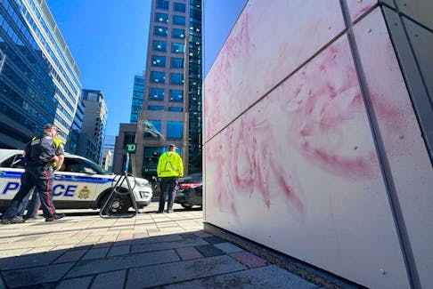 Ottawa police officers keep watch as crews clean anti-Israel grafitti painted on the office tower housing the Israeli embassy on O'Connor Street in downtown Ottawa, Ont. on Monday, April 15 2024.