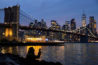 A person takes a photo while looking toward the Manhattan skyline on the Winter Solstice in Brooklyn, New York City, U.S., December 21, 2021.