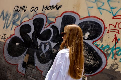 A woman walks past graffiti on the wall that says "tourist go home" in Las Palmas de Gran Canaria, Spain, April 13, 2024.