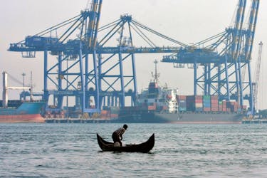 A fisherman prepares to cast his fishing net in the waters of the Vembanad lake as a container ship is seen docked in the background, at a port in Vallarpadam, in the southern Indian city of Kochi February 11, 2014.