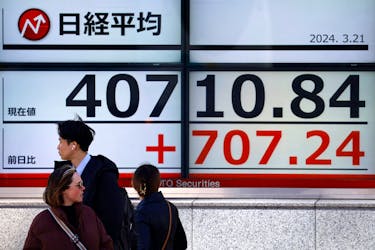 Passersby walk in front of an electric screen displaying Japan's Nikkei share average outside a brokerage in Tokyo, Japan March 21, 2024. 