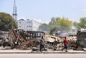 People walk past remains of vehicles near the presidential palace, after they were set on fire by gangs, as violence spreads and armed gangs expand their control over the capital, in Port-au-Prince, Haiti March 25, 2024.