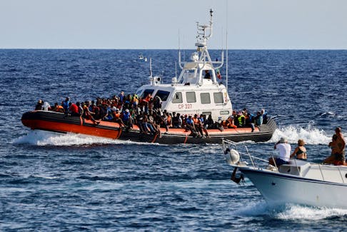 An Italian Coast Guard vessel carrying migrants rescued at sea passes near a tourist boat, on the Sicilian island of Lampedusa, Italy, September 18, 2023.