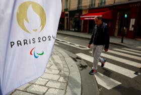 A man walks near a flag with the logo of the Paris 2024 Olympic and Paralympic Games in Paris, France, March 25, 2024.