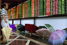 A Chinese investor monitors share prices in front of dozens of umbrellas left to dry at a Shanghai securities firm August 9, 2001./File Photo