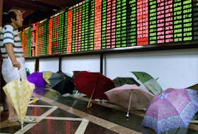 A Chinese investor monitors share prices in front of dozens of umbrellas left to dry at a Shanghai securities firm August 9, 2001./File Photo