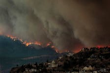Smoke and flames from wildfires serve as a backdrop for homes across Okanagan Lake in West Kelowna, British Columbia, Canada, August 17, 2023.