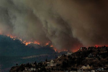Smoke and flames from wildfires serve as a backdrop for homes across Okanagan Lake in West Kelowna, British Columbia, Canada, August 17, 2023.