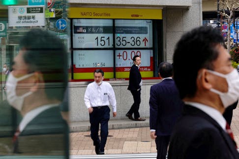 Pedestrians walk past an electric monitor displaying the Japanese yen exchange rate against the U.S. dollar outside a brokerage in Tokyo, Japan March 28, 2024.