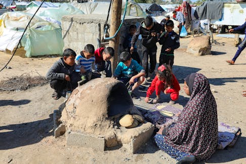 FIEL PHOTO: A Palestinian woman bakes bread as children sit next to her, while Gaza residents face crisis levels of hunger and soaring malnutrition, in Khan Younis in the southern Gaza Strip January 24, 2024.