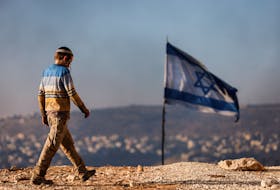 A Jewish settler teenager walks by an Israeli flag in Givat Eviatar, a new Israeli settler outpost, near the Palestinian village of Beita in the Israeli-occupied West Bank June 23, 2021. Picture taken June 23, 2021.