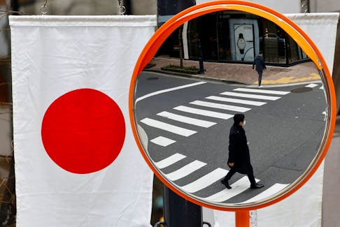 Pedestrians are reflected on a curved mirror next to Japan’s national flag in a shopping district in Tokyo, Japan March 19, 2024.