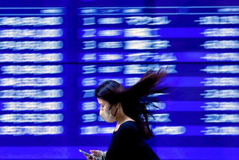 A passerby walks past an electric monitor displaying recent movements of various stock prices outside a bank in Tokyo, Japan, March 22, 2023.