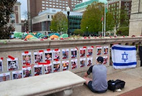 A person prays in front of photos of hostages posted on campus near an encampment where students are protesting in support of Palestinians at Columbia University, during the ongoing conflict between Israel and the Palestinian Islamist group Hamas, in New York City, New York, U.S., April 24, 2024.REUTERS/David 'Dee' Delgado/File Photo