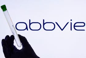 A woman holds a test tube in front of displayed Abbvie logo in this illustration taken, May 21, 2021.