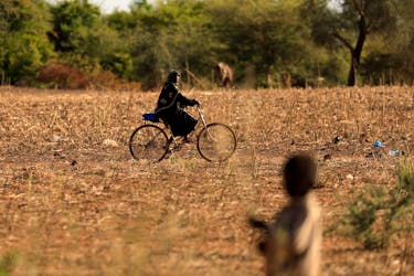 A child who fled with his parents from attacks of armed militants in the Sahel region watches a woman on a bicycle at a camp for internally displaced people (IDPs) in Kaya, Burkina Faso November 23, 2020. Picture taken November 23, 2020.