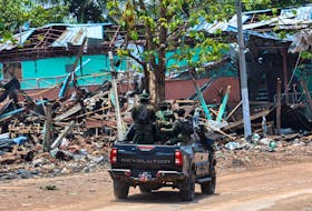 Soldiers from the Karen National Liberation Army (KNLA) patrol on a vehicle, next to an area destroyed by Myanmar's airstrike in Myawaddy, the Thailand-Myanmar border town under the control of a coalition of rebel forces led by the Karen National Union, in Myanmar, April 15, 2024.