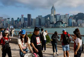 Mainland Chinese tourists walk in front of the skyline of buildings at Tsim Sha Tsui, in Hong Kong, China May 2, 2023.
