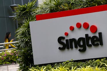 A woman using a mobile phone walks behind a Singtel signage at their head office in Singapore February 11, 2016. 