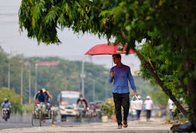 A man walks along a road with an umbrella to cover himself from the sun during a countrywide heatwave in Dhaka, Bangladesh, April 28, 2024.