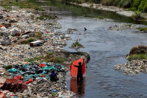 A man washes waste plastic sheets, collected for recycling, in polluted waters in Karachi, Pakistan June 5, 2023.