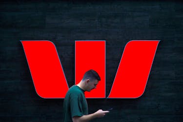 A pedestrian looks at his phone as he walks past a logo for Australia's Westpac Banking Corp located outside a branch in central Sydney, Australia, November 5, 2018.
