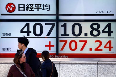 File photo: Passersby walk in front of an electric screen displaying Japan's Nikkei share average outside a brokerage in Tokyo, Japan March 21, 2024. 