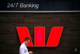 A pedestrian looks at his phone as he walks past a logo for Australia's Westpac Banking Corp located outside a branch in central Sydney, Australia, November 5, 2018.  