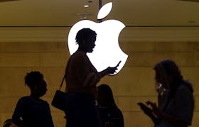 A women uses an iPhone mobile device as she passes a lighted Apple logo at the Apple store at Grand Central Terminal in New York City, U.S., April 14, 2023.