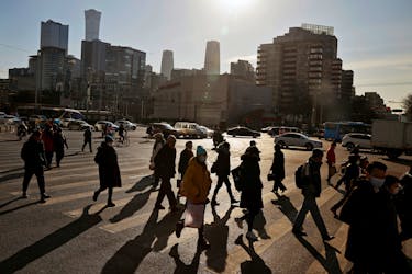 People cross a street during morning rush hour in front of the skyline of the central business district (CBD) in Beijing, China December 15, 2020.