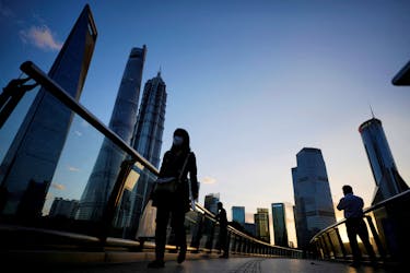 People walk on an overpass past office towers in the Lujiazui financial district of Shanghai, China October 17, 2022.