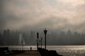 A person stands on the Hudson River shoreline as heavy fog hangs over the skyline of New York City and midtown Manhattan in the background, in Weehawken, New Jersey, U.S., February 27, 2024.