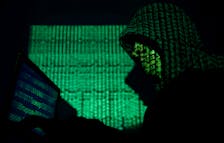 A hooded man holds a laptop computer as cyber code is projected on him in this illustration picture taken on May 13, 2017.