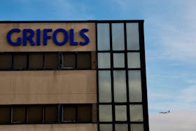 A plane flies behind an office and logistics building of Spanish pharmaceuticals company Grifols in Coslada, near Madrid, Spain, January 9, 2024.