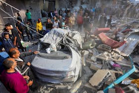 Palestinians gather near the remains of a car at the site of an Israeli strike on a house, amid the ongoing conflict between Israel and the Palestinian Islamist group Hamas, in Nuseirat refugee camp in the central Gaza Strip, May 14, 2024.