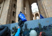 A demonstrator wearing a European Union flag climbs a fence protecting the gates of the parliament building during a rally to protest against a bill on "foreign agents" in Tbilisi, Georgia, May 14, 2024.