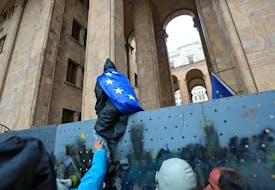 A demonstrator wearing a European Union flag climbs a fence protecting the gates of the parliament building during a rally to protest against a bill on "foreign agents" in Tbilisi, Georgia, May 14, 2024.