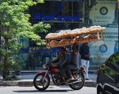 Egyptian street vendors carrying breads, drive past a currency exchange point, displaying images of the U.S. dollar, in Cairo, Egypt May 9, 2024.