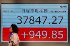 A passerby walks past in front of an electric screen displaying Japan's Nikkei share average outside a brokerage in Tokyo, Japan February 13, 2024. 