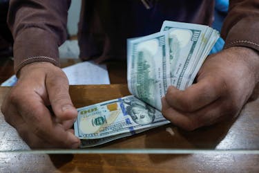 An employee of a foreign exchange shop counts U.S. dollar banknotes from behind a glass booth in Karachi, Pakistan September 7, 2023.