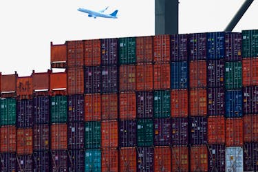 Shipping containers are seen stacked on a docked cargo ship as a passenger airplane takes off from Newark Airport, in Port Elizabeth, New Jersey, U.S., July 12, 2023.