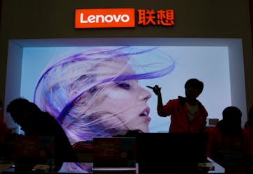 An employee gestures next to a Lenovo logo at Lenovo Tech World in Beijing, China November 15, 2019.