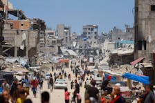 People and vehicles pass by buildings destroyed in an Israeli strike, amid the ongoing conflict between Israel and Hamas, in Khan Younis, in the southern Gaza Strip, May 22, 2024.