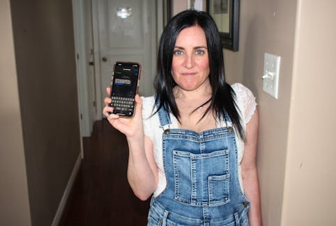 Tracy Tucker stands in her South Bar home on Thursday, May 23, holding her phone with the text message that a scammer used in attempts to defraud her. NICOLE SULLIVAN / CAPE BRETON POST