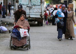A Palestinian man assists a woman in a wheel chair carrying her belongings as they travel to flee Rafah due to an Israeli military operation, in Rafah, in the southern Gaza Strip, May 28, 2024.