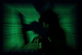 A  hooded man holds laptop computer as cyber code is projected on him in this illustration picture taken on May 13, 2017.