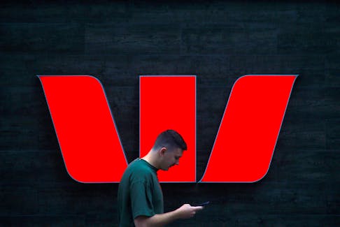 A pedestrian looks at his phone as he walks past a logo for Australia's Westpac Banking Corp located outside a branch in central Sydney, Australia, November 5, 2018.