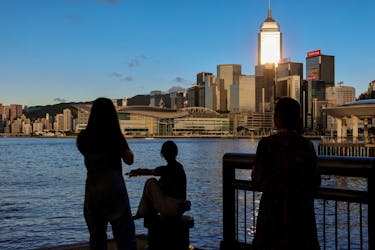 Tourists relax by the Victoria Harbour waterfront, with the iconic skyline providing a scenic backdrop, in Hong Kong, China, July 10, 2023.