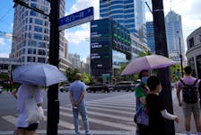 Pedestrians wait to cross a road at a junction near a giant display of stock indexes in Shanghai, China August 3, 2022.