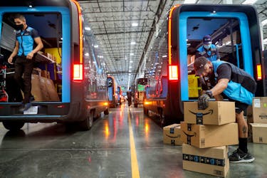 Workers load packages into Amazon Rivian electric trucks at an Amazon facility in Poway, California, U.S., November 16, 2022. 
